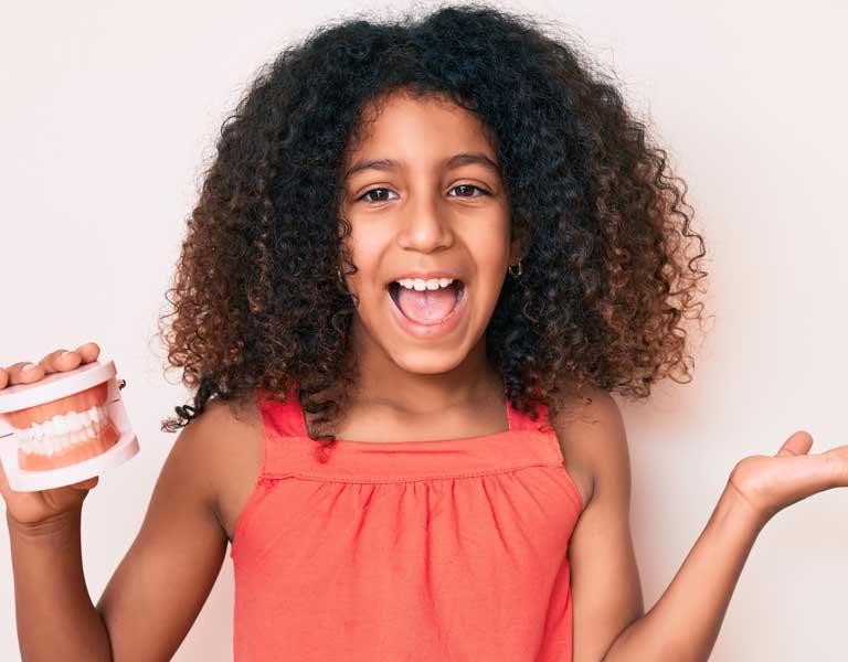 African-American child with curly hair holding a denture at a dental clinic in Stafford, VA