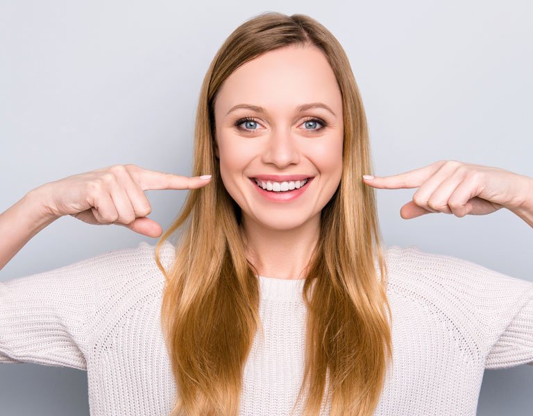 A woman pointing to her teeth at a dental clinic in Stafford, VA