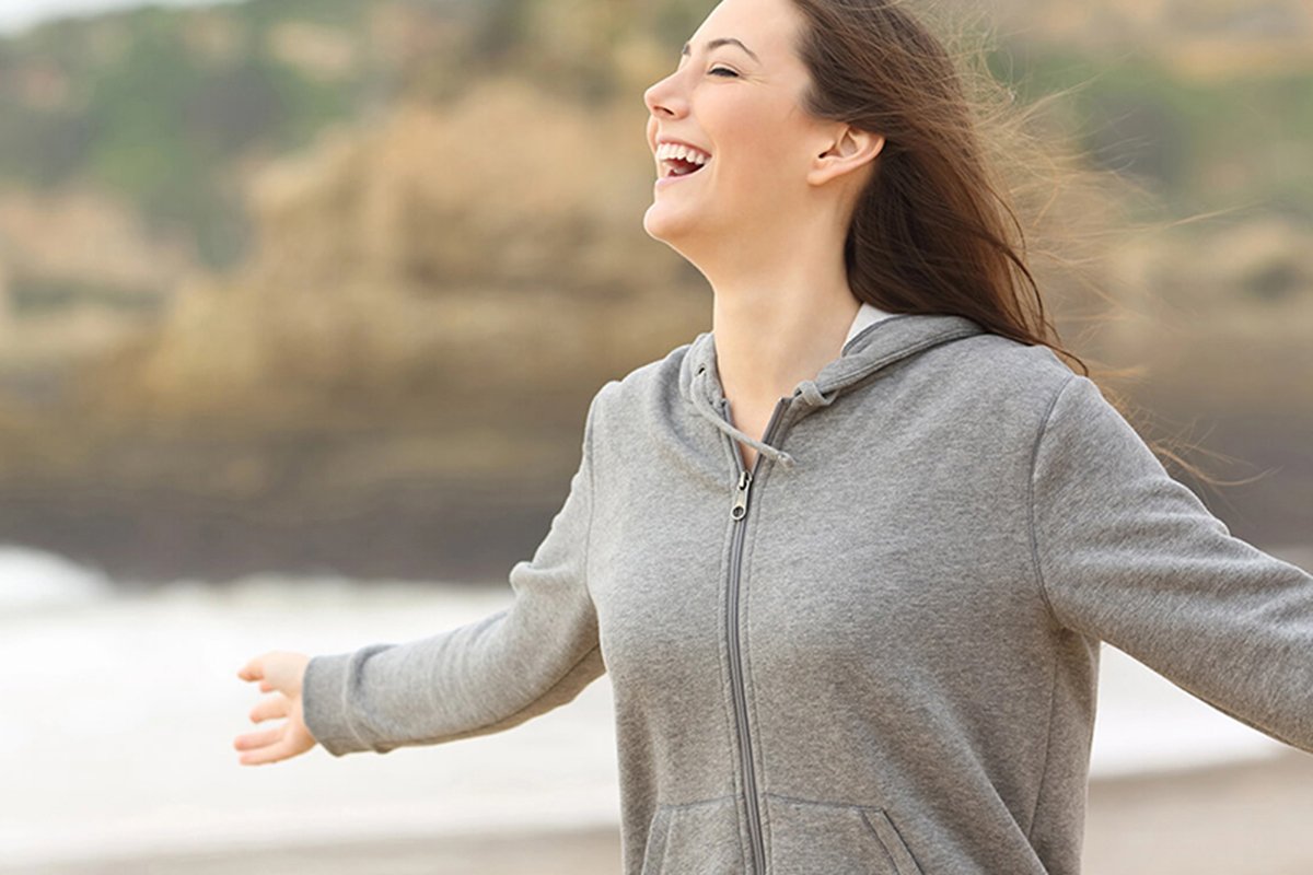 Person in gray hoodie with arms outstretched near seaside, symbolizing holistic biological dentistry in Stafford, VA